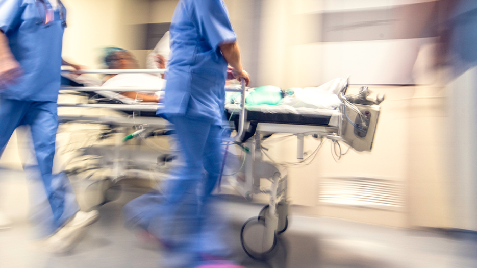 Blurred image of healthcare workers running and pushing a patient on a gurney down a hall.